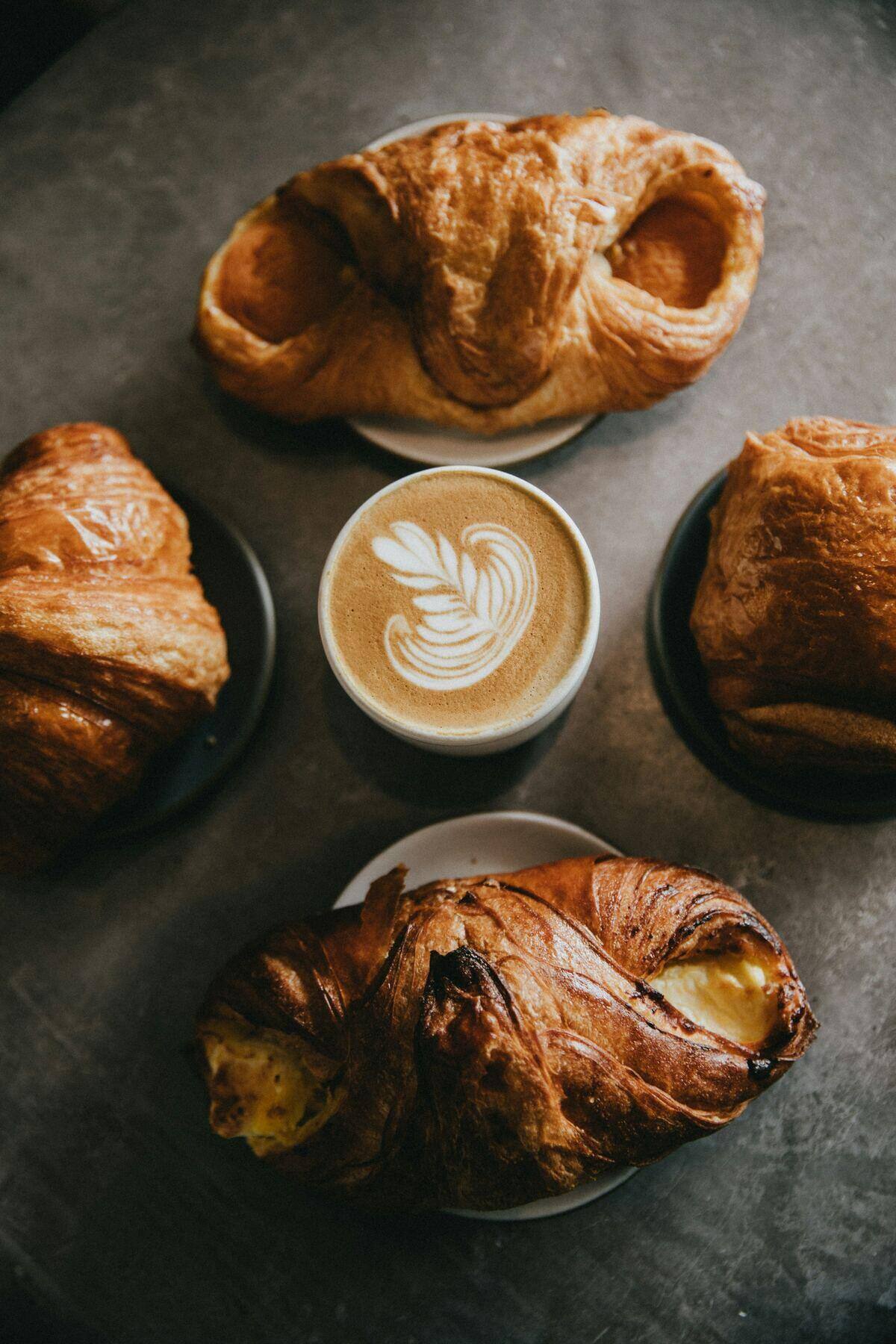 Four croissants arranged around a cup of coffee with leaf art